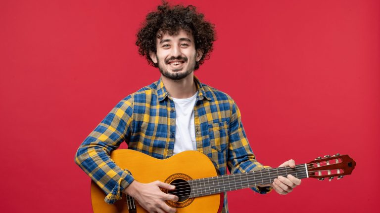 front-view-young-male-playing-guitar-red-wall-for music website